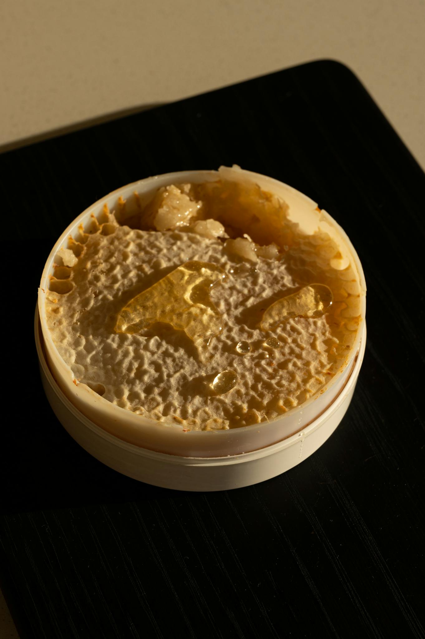 Close-up of a honey comb in a round plastic container on a black surface.
