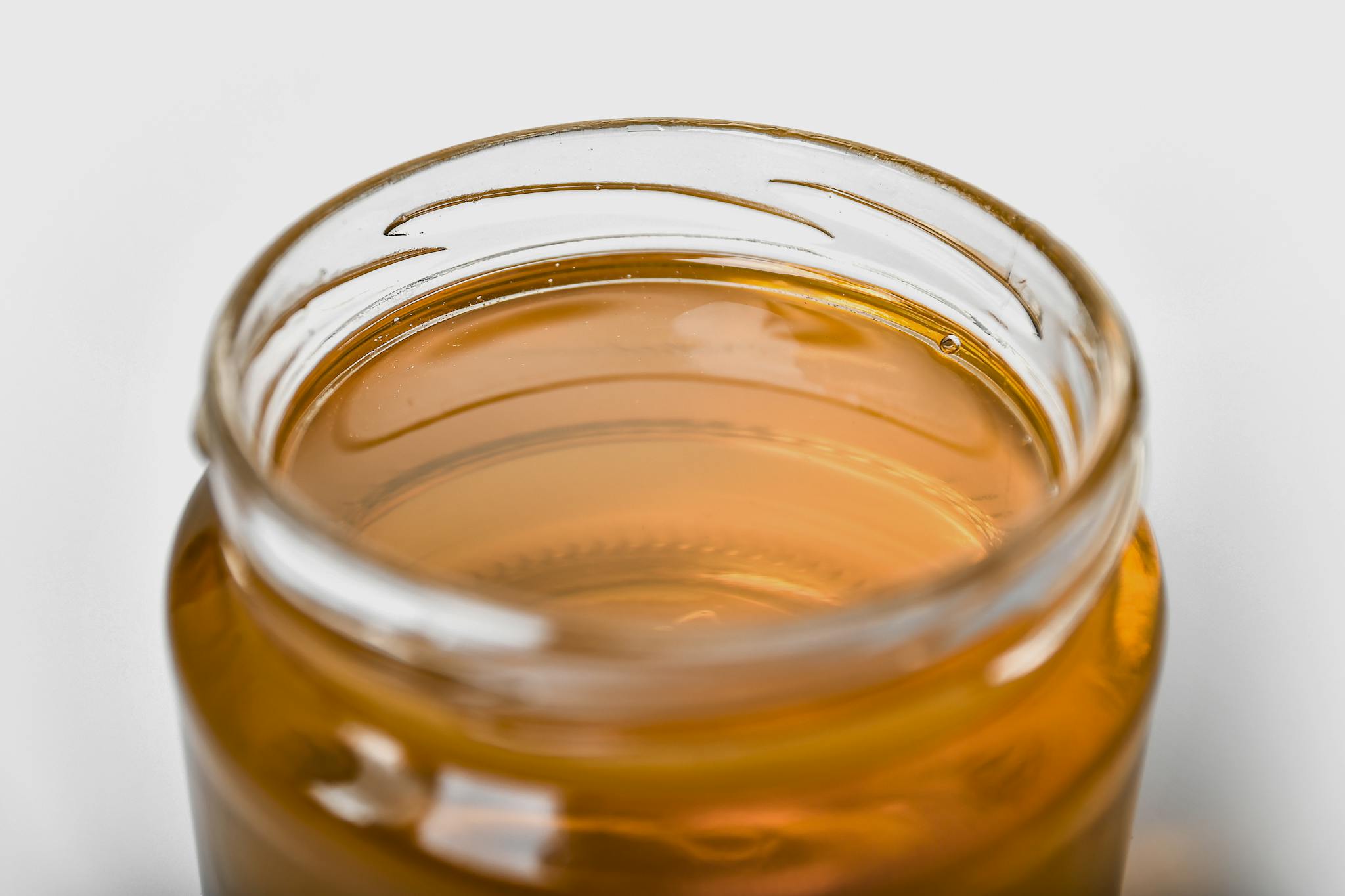 Close-up of a jar filled with golden honey, emphasizing its smooth texture and shimmering hue.